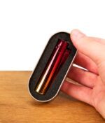 Eine Hand hält das geöffnete silberne Metalletui (Geschenkbox), in dessen passgenauem schwarzen Schaumstoff-Inlay das Clipper Metall Sunset Gradient sicher verstaut ist.
