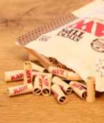 Vorgedrehte Filtertips mit rotem Logo aus dem RAW Sticky Tips 100er Pack im Detail auf einer Holzoberfläche.