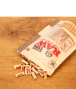 Liegende RAW Sticky Tips 100er Pack Packung mit auf einer Holzoberfläche herabgefallenen, vorgedrehten Filtertips.