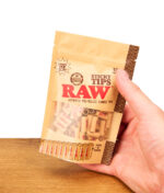 RAW Sticky Tips 100er Pack Beutel mit vorgedrehten Filtertips, von einer Hand über einer Holzoberfläche gehalten.