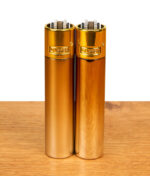 Clipper Metall Gradient Elegance Feuerzeuge im 2er-Set mit mattem und glänzendem Gold-Finish nebeneinander auf Holz.