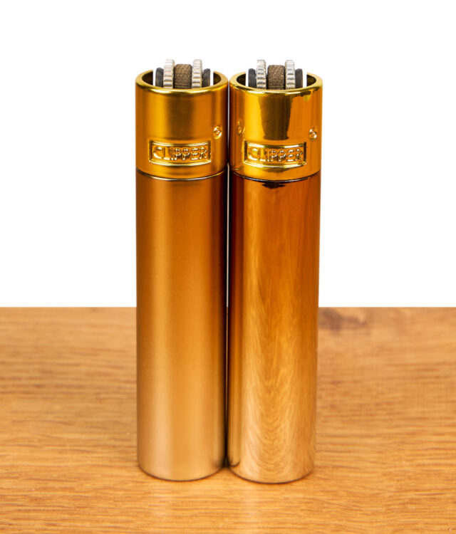 Clipper Metall Gradient Elegance Feuerzeuge im 2er-Set mit mattem und glänzendem Gold-Finish nebeneinander auf Holz.
