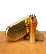 Glänzendes Clipper Metall Gradient Elegance Gold Feuerzeug neben geprägter Metalldose und Stein auf Holz.