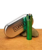 Glänzendes Clipper Metall Turquoise Feuerzeug stehend neben einer geprägten Metalldose und einem Stein auf Holz.