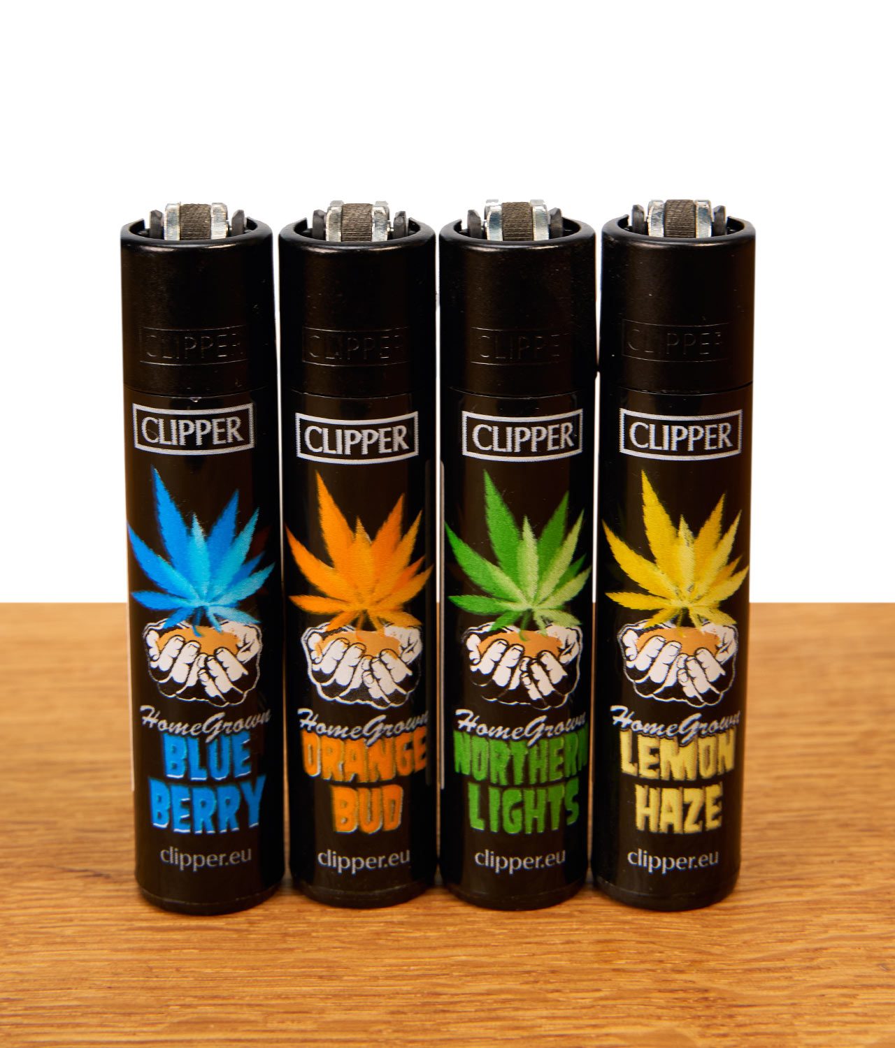 clipper-feuerzeug-serie-homegrown-4er-set Clipper HomeGrown 4er-Set wiederbefüllbare Reibradfeuerzeuge in Schwarz mit bunten Hanfblatt-Motiven bekannter Cannabis-Sorten auf Holz.