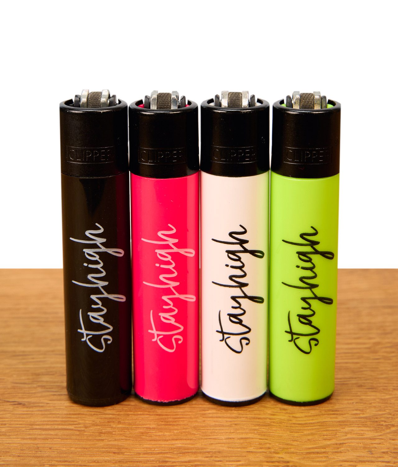 clipper-stayhigh-4er-serie-jpg Clipper Stayhigh 4er-Set wiederbefüllbare Reibradfeuerzeuge in Schwarz, Pink, Weiß und Neongrün mit geschwungenem Schriftzug auf Holz.