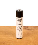 Weißes Clipper-Feuerzeug Adult #1 auf Holz mit schwarzem Metall-Zündrad und Grafik-Aufdruck "Lick it Good".