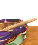 Nahaufnahme eines Joints, der in der Einkerbung des schillernden GRAV Ellipse Aschenbechers aus massivem Glas auf Holz liegt.