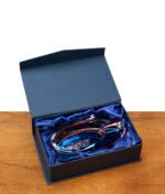 Der schillernde GRAV Ellipse Glas-Aschenbecher eingebettet in blauem Satinstoff in einer geöffneten Premium-Geschenkbox.