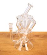 MJ Arsenal Triad Mini Rig Dab Rig aus Glas mit schwarzem Marken-Logo auf der runden Basis auf Holz.