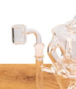 Nahaufnahme des klaren Quarz-Bangers am geschliffenen Anschluss des MJ Arsenal Triad Mini Rigs auf Holz.