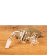 Quarz-Banger und gläserne Carb Cap des MJ Arsenal Triad Mini Rigs liegend auf Holz vor einem Stein.