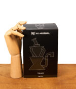 Schwarze MJ Arsenal Triad Mini Rig Produktbox neben einer hölzernen Gliederhand auf einem Tisch.