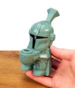 In der Hand gehaltene Space Hero Silikon Bong in Kopfgeldjäger-Optik über Holzoberfläche, modularer Körper ohne Glaskopf.