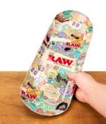 In der Hand gehaltenes RAW x Chris Psiacik Skate Deck Rolling Tray aus Metall über einer rustikalen Holzoberfläche.