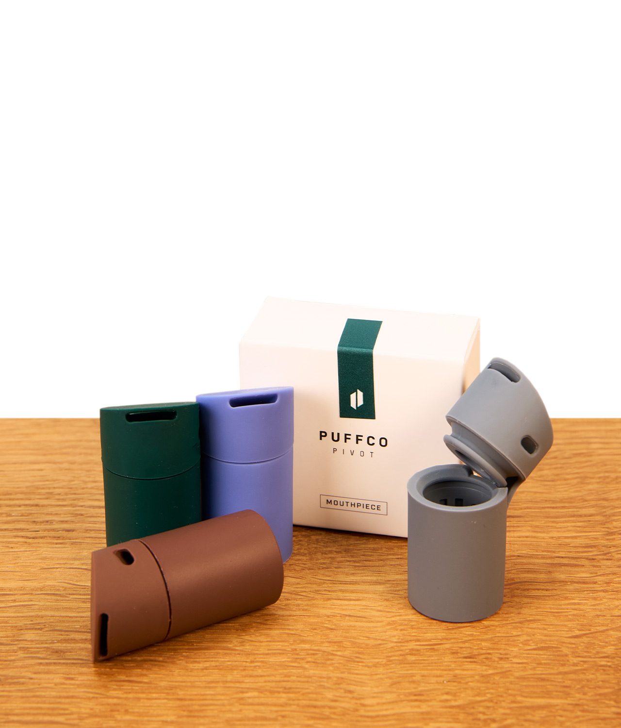 puffco-pivot-mundstuecke-gruppenbild-jpg Puffco Pivot Mundstück Set in vier Farben samt Originalverpackung auf Holz dekoriert, das graue Silikonteil ist geöffnet.