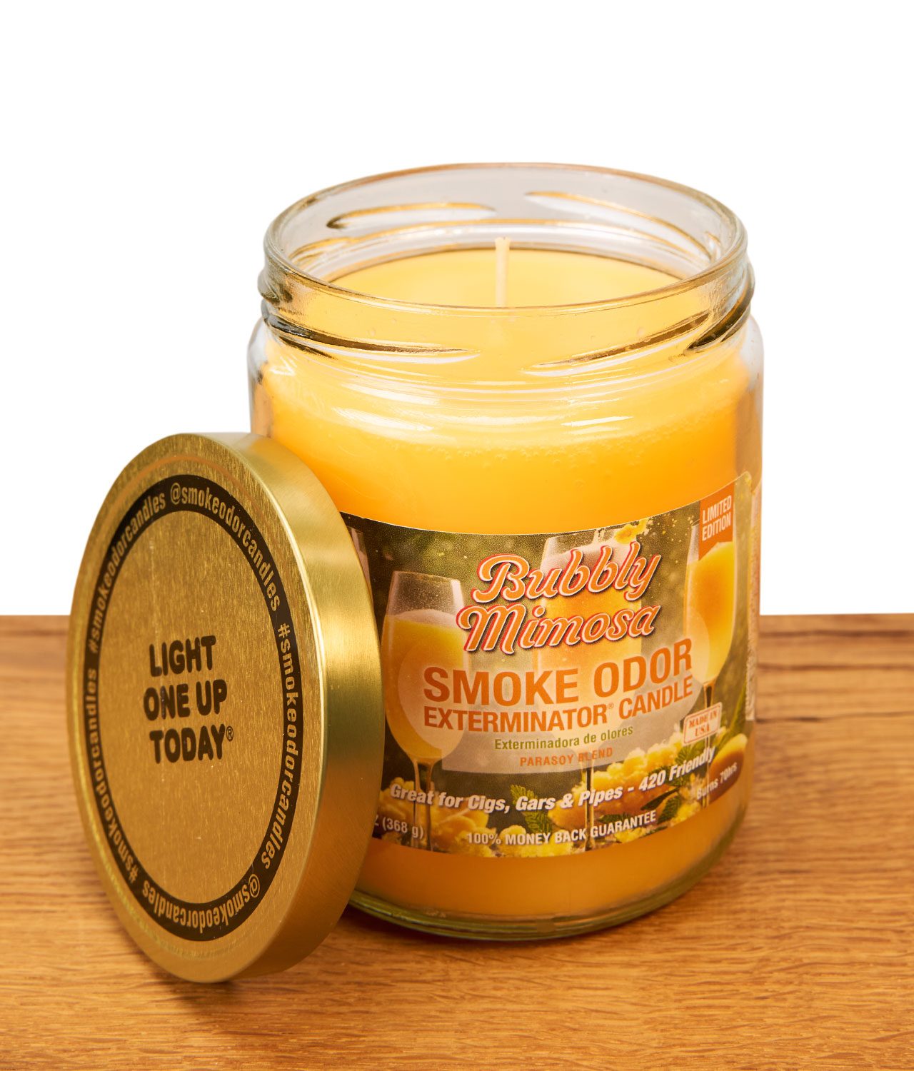 smoke-odor-limited-edition-bubbly-mimosa-1-jpg Geöffnete Smoke Odor Bubbly Mimosa Kerze im Glas mit angelehntem goldenen Metalldeckel auf einer Holzoberfläche.
