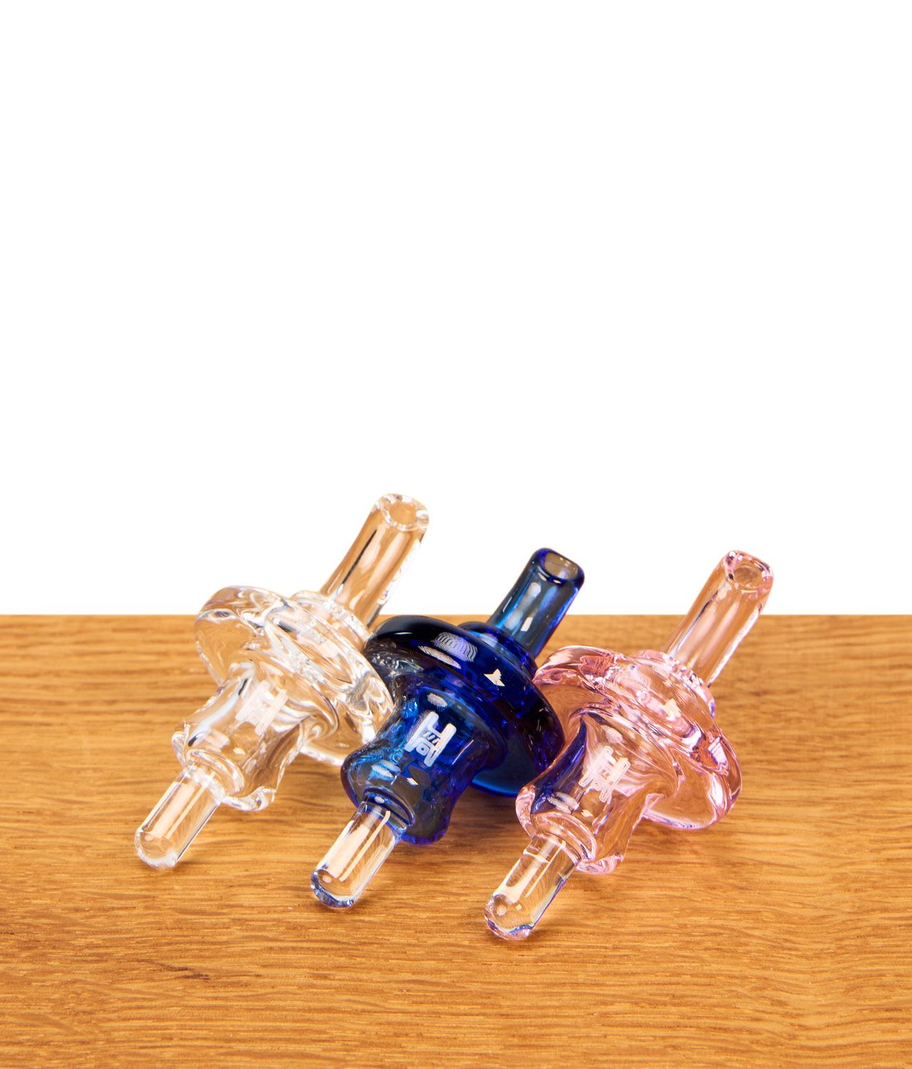 human-grade-directional-carb-cap-3er-set-jpg Human Grade Directional Carb Cap im 3er-Set aus Borosilikatglas in den Farben Klar, Blau und Rosa auf Holztisch.