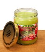 Geöffnete Smoke Odor Exterminator Candle Watermelon Zlushie. Glas mit grünem Wachs und angelehntem goldenen Deckel auf Holz.