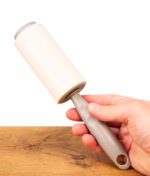 Hand umschließt den ergonomischen grauen Kunststoffgriff des unauffälligen Buddies Fusselroller Safe in aufrechter Position.
