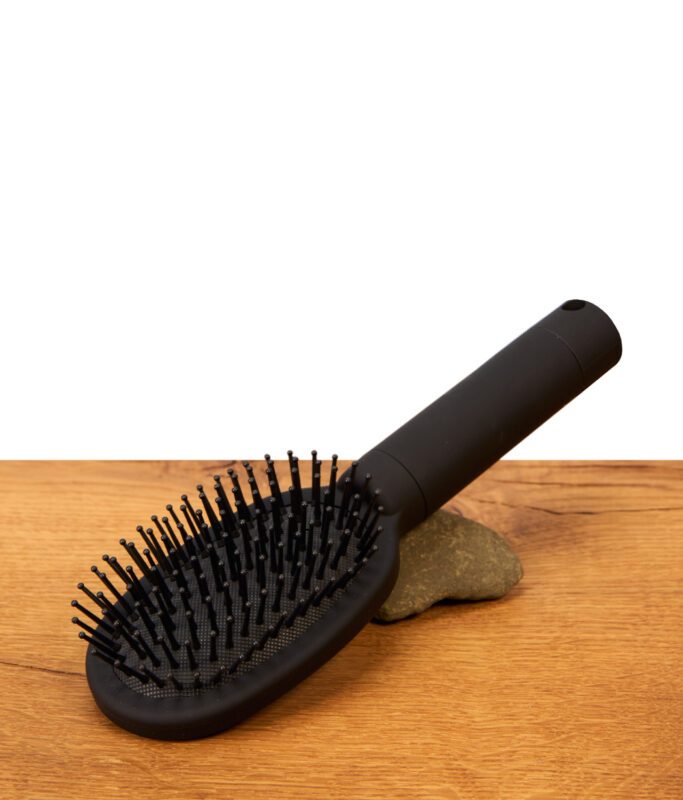 Voll funktionsfähiger Buddies Hairbrush Safe liegend auf einem Holztisch. Mattschwarze Haarbürste aus Kunststoff mit intakten Borsten.