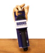 Hölzerne Gliederhand hält den mattschwarzen Buddies Hairbrush Safe in originaler blau-weißer Kartonverpackung auf einem Holztisch.