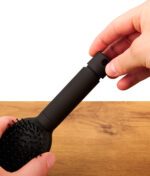 Hände öffnen den Schraubverschluss am Griff des mattschwarzen Buddies Hairbrush Safe. Detailaufnahme des Kunststoff-Verstecks über einem Holztisch.