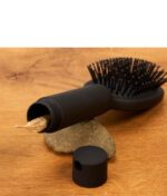 Geöffneter Buddies Hairbrush Safe auf einem Holztisch. Ein Joint ragt aus dem zylindrischen Geheimfach im schwarzen Kunststoffgriff.