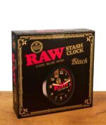 Originalverpackung der RAW Black Stash Clock auf Holztisch. Schwarzer Karton der Versteckuhr mit goldener Schrift und rotem Markenlogo.
