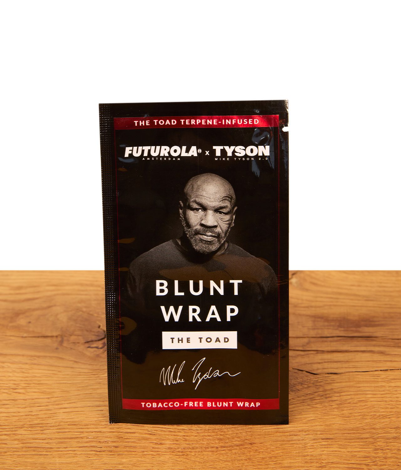 futurola-mike-tyson-blunt-wrap-jpg Futurola x Tyson 2.0 The Toad Blunt Wrap Verpackung aus glänzender Folie mit Mike-Tyson-Aufdruck auf einem Holztisch.