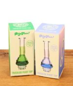 Originalverpackungen des BigFun! Tricolor Pivot Top für Puffco Pivot Vaporizer in Grün und Blau auf einem Holztisch.