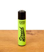 Neongrünes Clipper Feuerzeug Stoned mit schwarzem Schreibschrift-Design auf Holztisch, wiederbefüllbares Nylon-Gasfeuerzeug.