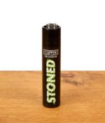 Schwarzes Clipper Feuerzeug Stoned Glitch mit grünem Schriftzug auf Holztisch, nachfüllbares Nylon-Gasfeuerzeug mit Zündstein.