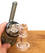 Hand hält Glass-Dab-Rig mit montiertem Human Grade 10mm Terp Slurper Quarzbanger über Holztisch.